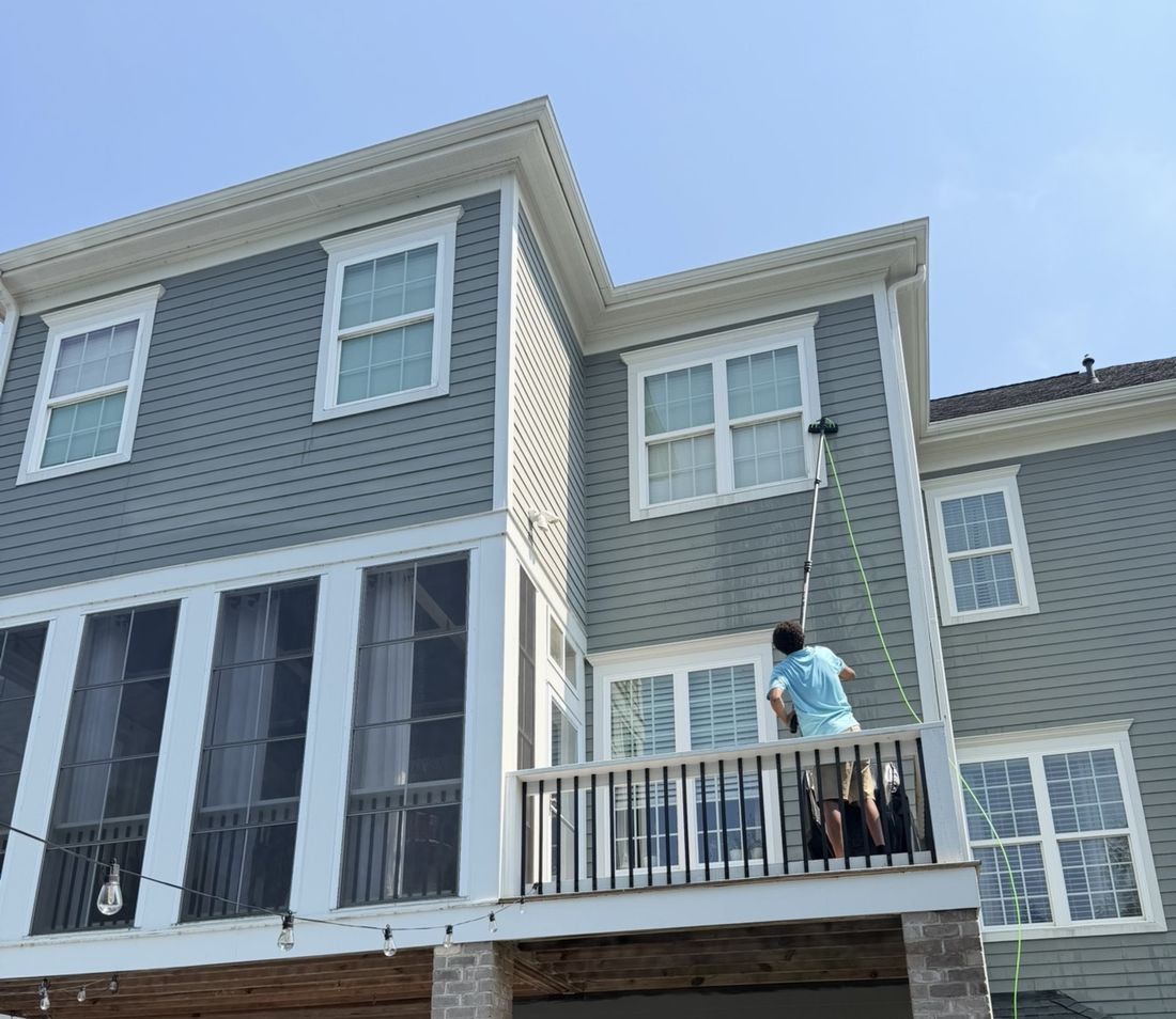 Webz technician cleaning a third-story window with a water-fed pole, no ladder
